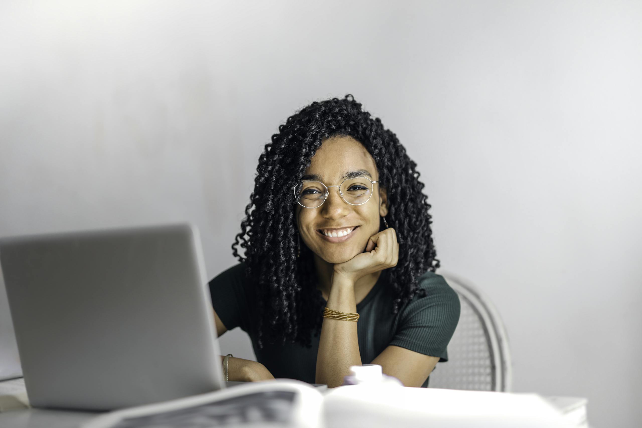 Happy ethnic woman sitting at table with laptop